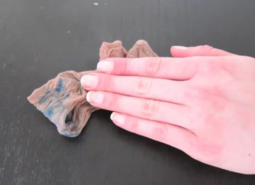Hand cleaning a dark surface with a brown cloth, revealing a blue stain.