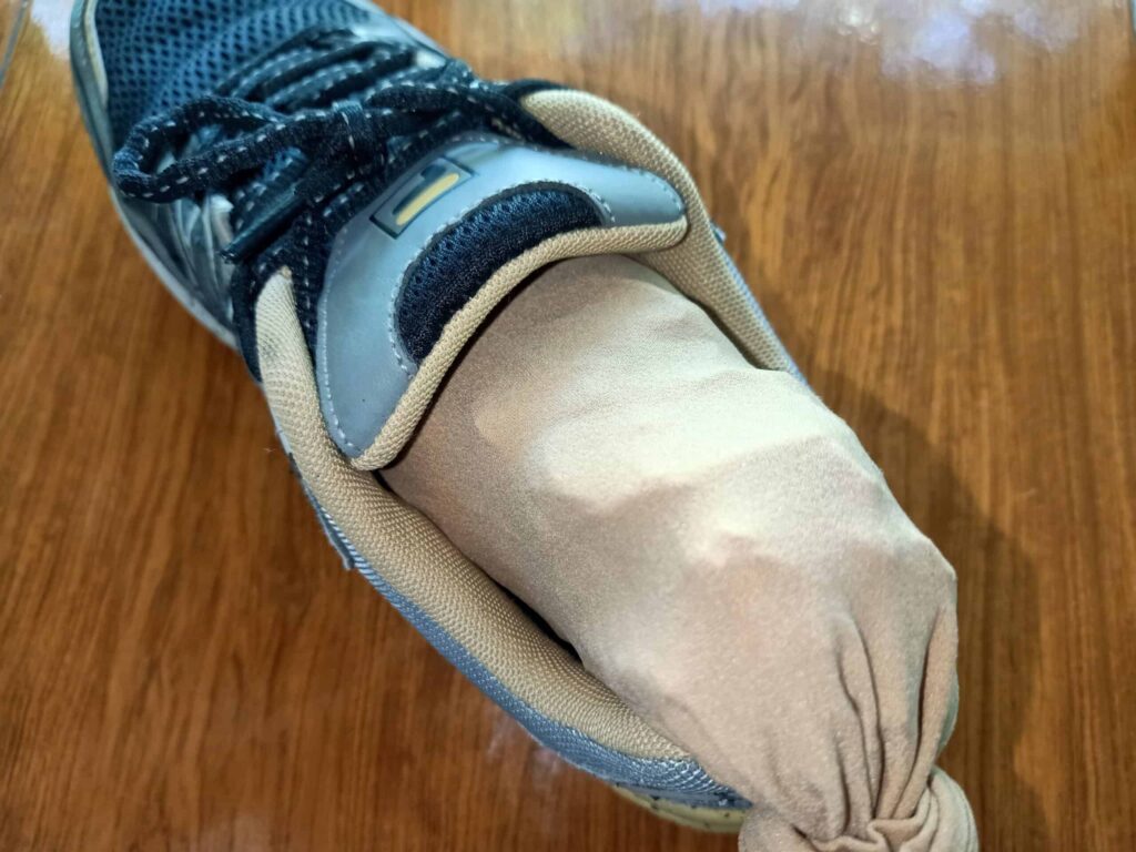 A black and gray sneaker with a rolled-up beige sock stuffed inside, placed on a wooden surface.