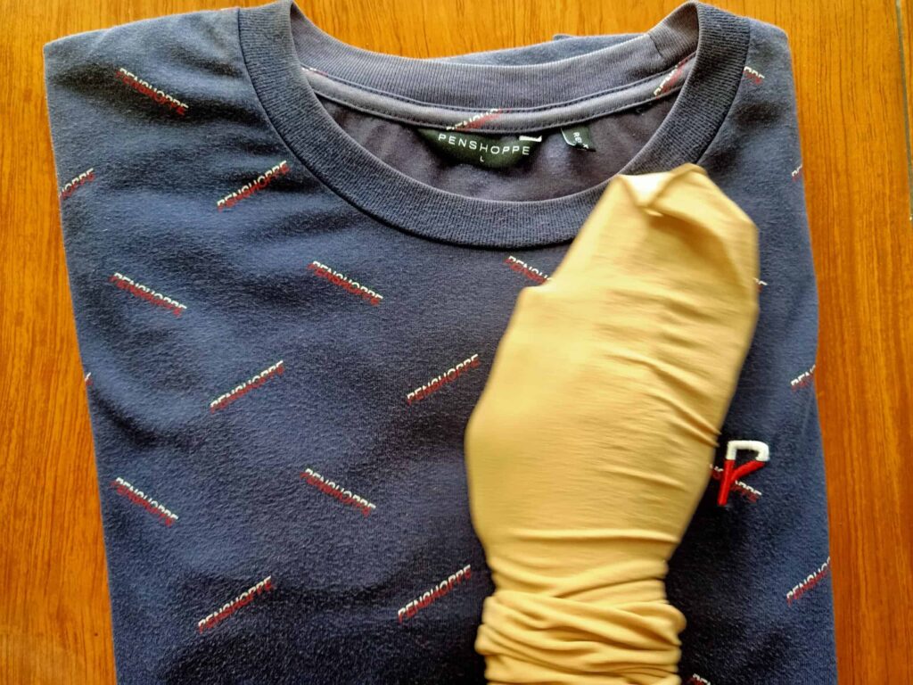 A folded blue shirt with a patterned design is placed on a wooden surface. A gloved hand is visible in the foreground.