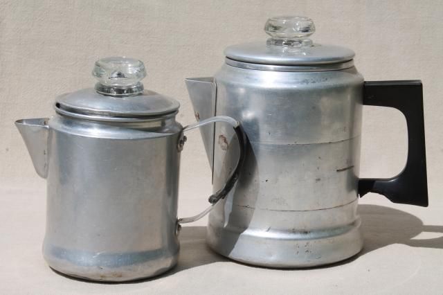 Two metal kettles with glass lids; the smaller has a spout and a handle, while the larger has a black handle. Both are placed on a neutral background.