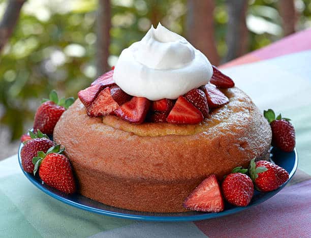 Strawberry shortcake with sliced strawberries and whipped cream topping on a blue plate, set on a colorful tablecloth.
