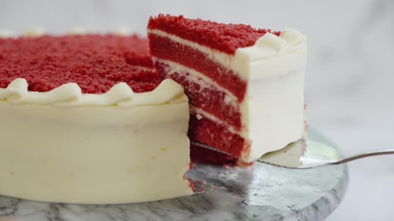 A slice of red velvet cake with cream cheese frosting is being lifted from the whole cake on a marble surface.