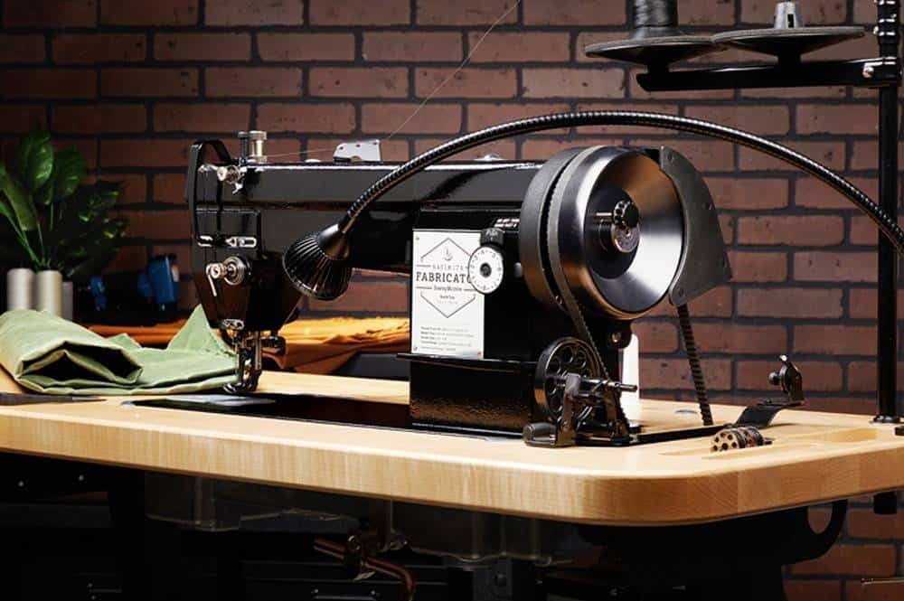 Industrial sewing machine on a wooden table, with fabric and a brick wall backdrop.