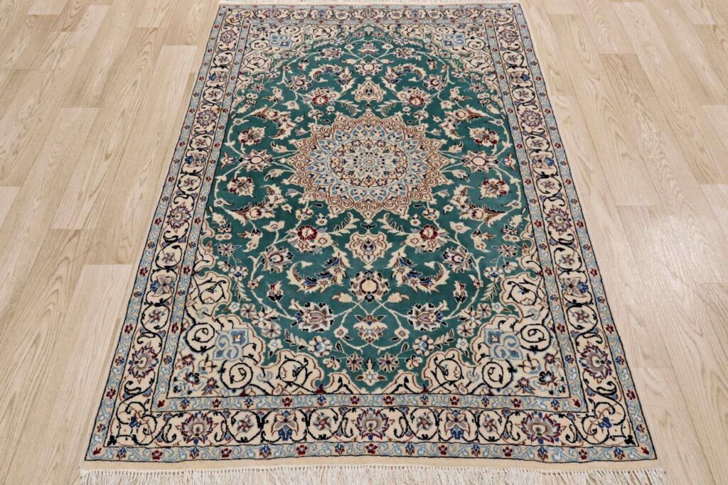 Intricately patterned rug with a central medallion, featuring floral and geometric designs in green, cream, and blue hues on a wooden floor.