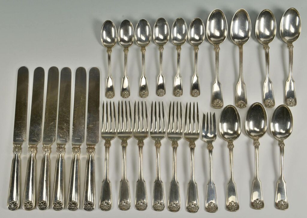 A neatly arranged set of silverware includes six knives, six forks, six large spoons, and six small spoons, all with ornate handles.
