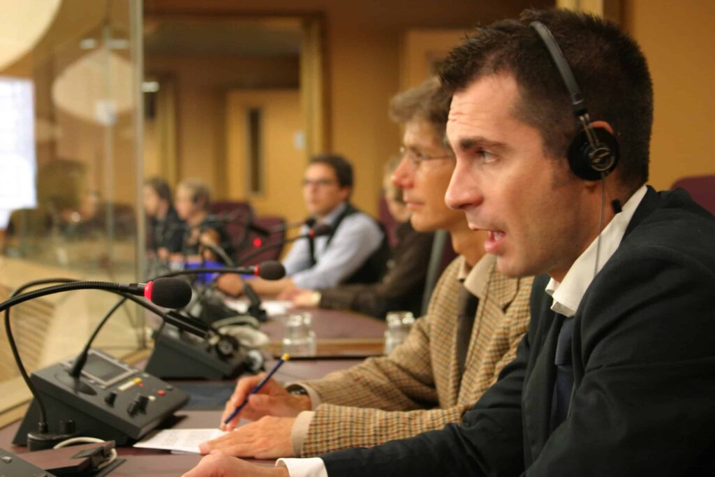 People wearing headsets sit at a conference table with microphones and papers in front of them.