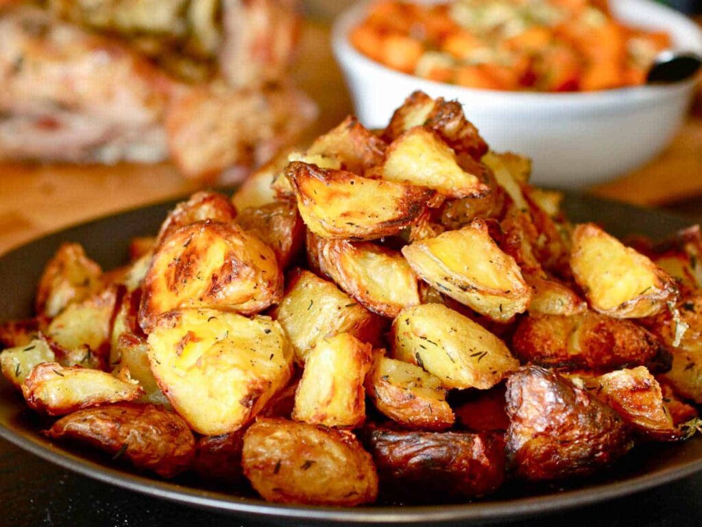 A plate of roasted potatoes is stacked high, with a bowl of vegetables in the background.