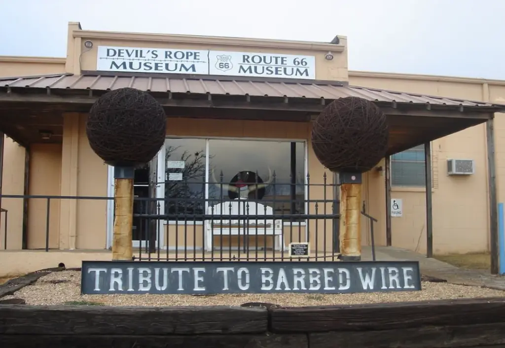 Exterior view of the Devil's Rope Museum featuring two large barbed wire sculptures and a "Tribute to Barbed Wire" sign.
