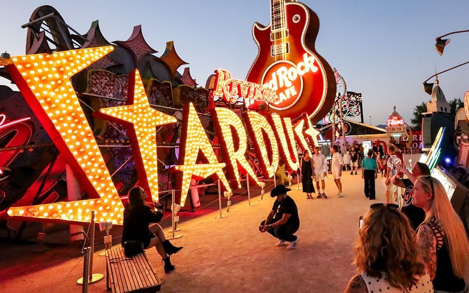 Visitors explore a neon sign exhibit with large "Stardust" letters and a Hard Rock Cafe guitar during early evening.