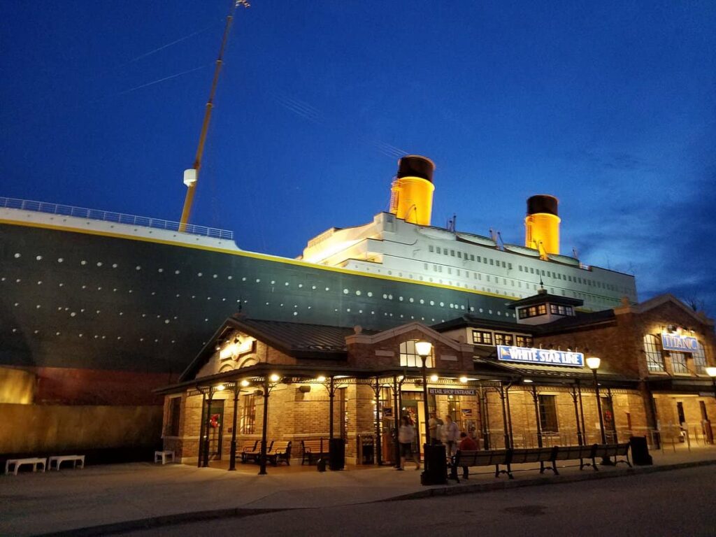 Exterior view of a brick building labeled "White Star Line" with a large ship replica in the background under a twilight sky.