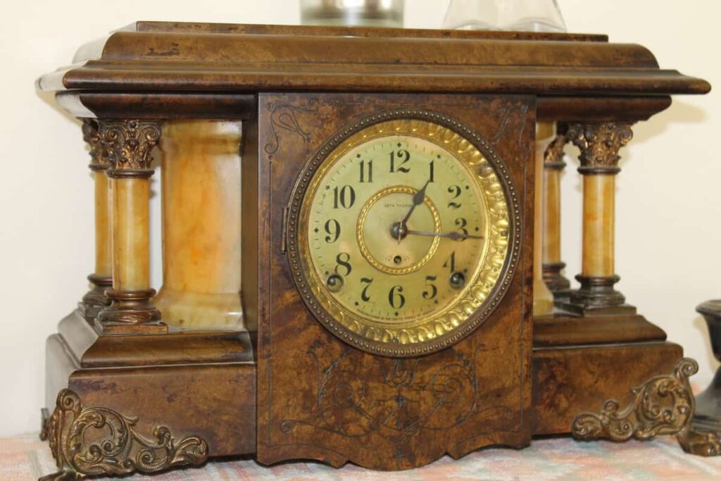 An ornate vintage mantel clock with Roman numerals and decorative pillars on each side, set on a textured surface.