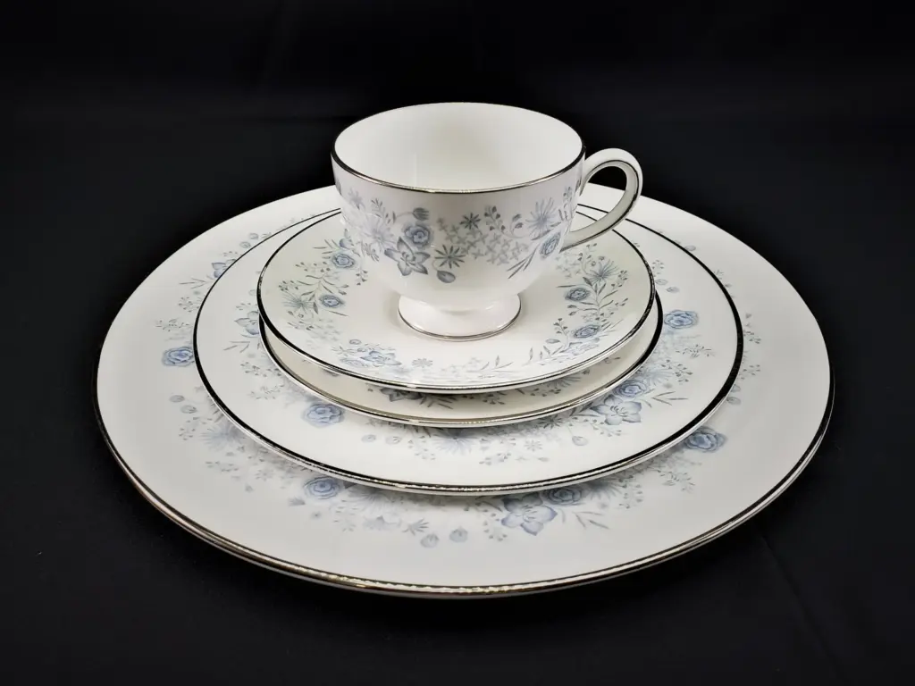 A stack of white porcelain dishes with blue floral patterns, including a teacup, saucer, and three plates, against a black background.