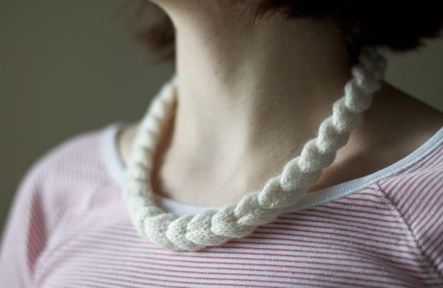 A person wears a white braided necklace over a pink and white striped shirt.