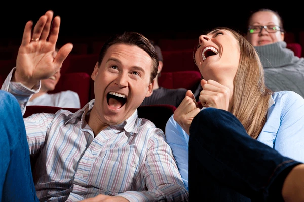 A man and woman are laughing joyfully together in a theater, surrounded by other seated people.
