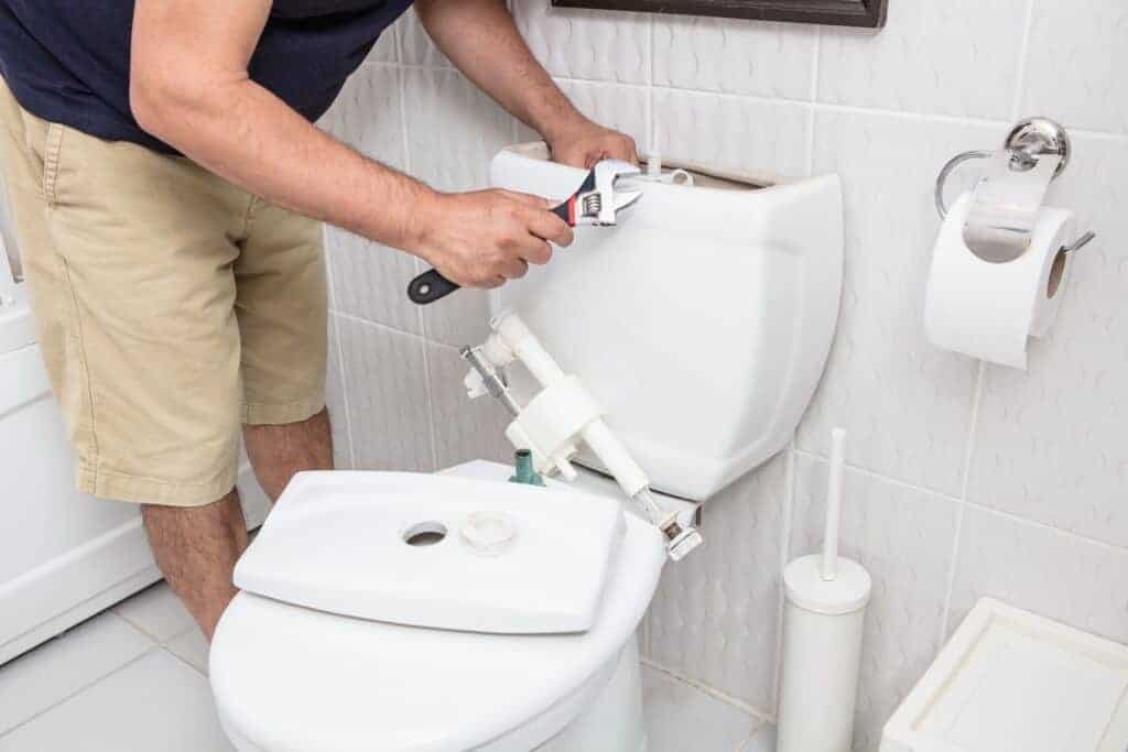Person using a wrench to repair a toilet tank in a bathroom.