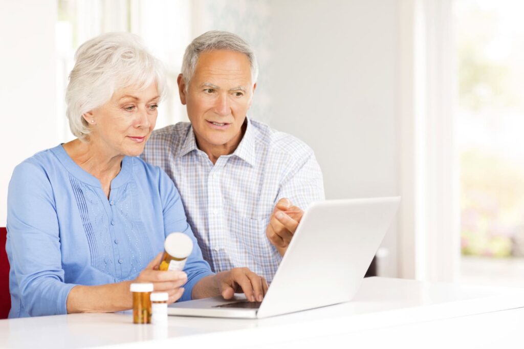 Older couple looking at a laptop together with medication bottles nearby.