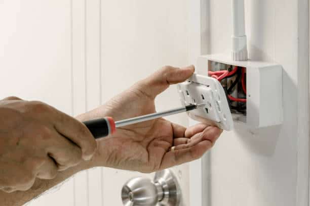 A person uses a screwdriver to install an electrical outlet cover on a wall.