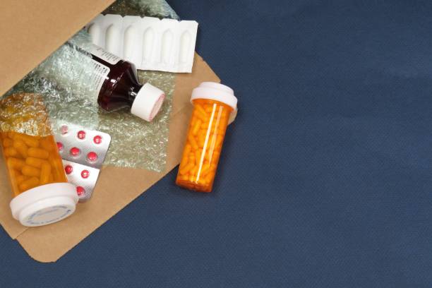 Open mailing envelope with pill bottles, blister packs, and medicine on a dark surface.