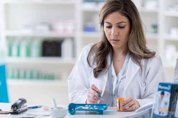 Pharmacist counting pills using a tablet counter in a pharmacy setting.