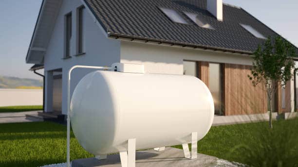 White propane tank in front of a modern house with a sloped roof and large windows, set on a green lawn.