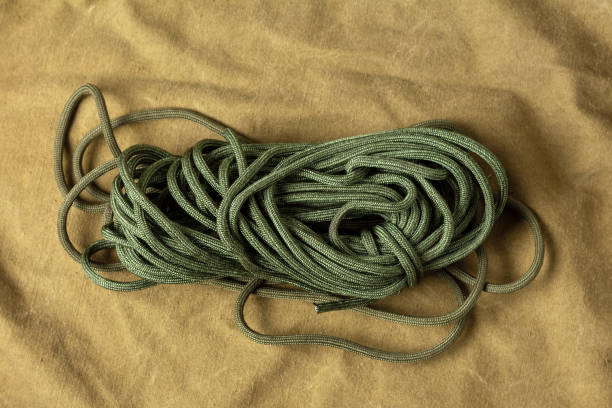 A coiled green rope is lying on a light brown fabric surface.