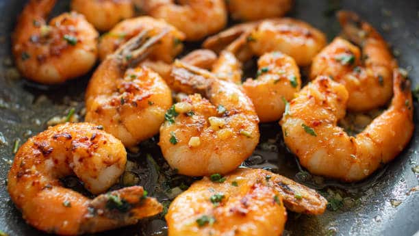 Close-up of cooked shrimp seasoned with herbs and spices in a pan.