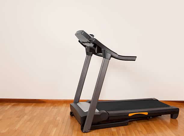 A treadmill on a wooden floor against a plain wall.
