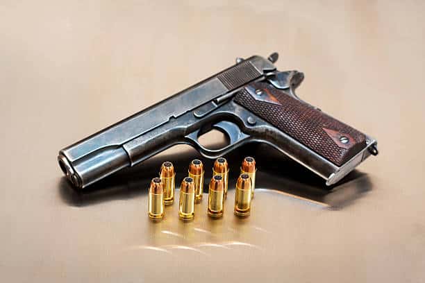 A handgun placed on a surface with seven bullets lined up in front of it.