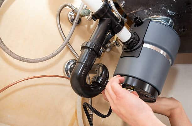Person installing a garbage disposal unit under a kitchen sink.