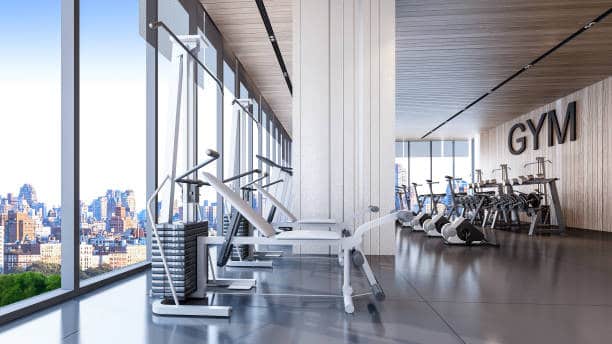 Modern gym interior with exercise equipment and large windows overlooking a city skyline.