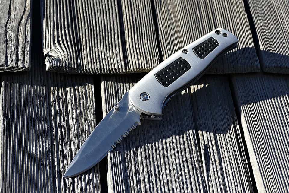 A folding pocket knife with a partially serrated blade rests on a wooden surface.