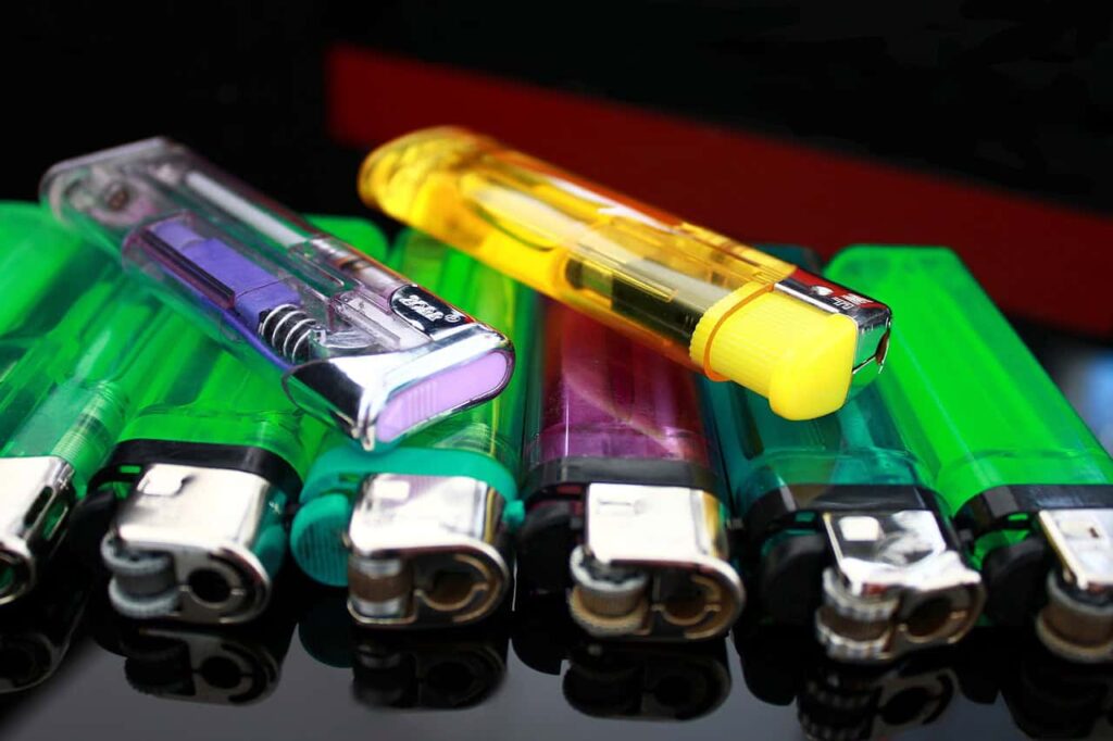 A row of colorful, transparent plastic lighters, including green, yellow, and purple, displayed on a reflective surface.