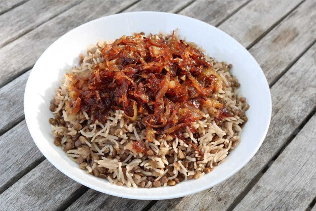 A bowl of rice and lentils topped with caramelized onions on a wooden table.
