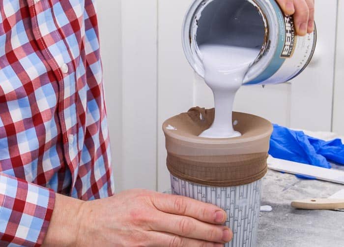 Person pouring white paint from a can into a container with a strainer on top.