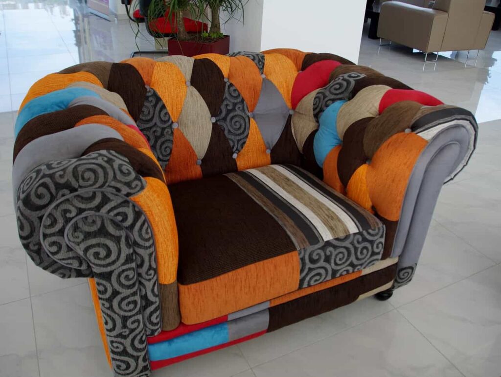 A colorful patchwork armchair with various geometric patterns and textures, set on a light-tiled floor in a modern interior space.