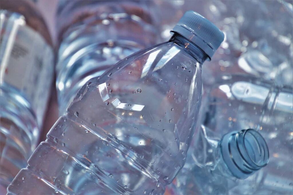 Close-up of several clear plastic water bottles, some with caps on and some without. Droplets of water are visible on the surface of one of the bottles.