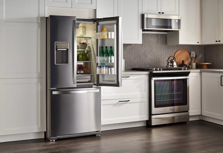 Modern kitchen with a stainless steel fridge, open to reveal contents, next to a stove and microwave. White cabinets and dark wood flooring complete the look.
