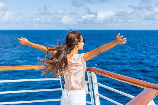 A woman with long hair stands on a ship's deck, facing the sea with arms outstretched.