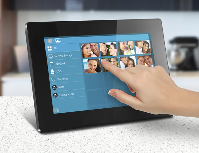 A hand interacts with a digital photo frame displaying a collection of family photos, with storage options like internal, SD card, and USB visible on the screen.