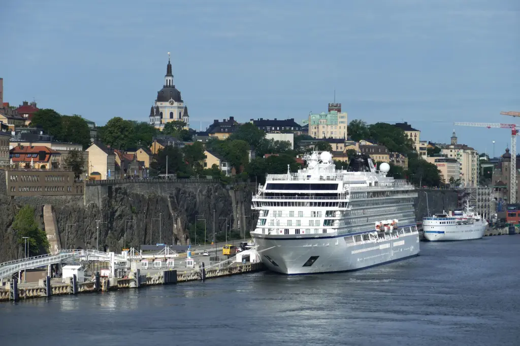 Cruise ships docked beside a rocky shoreline in a city with historic buildings and a church in the background.