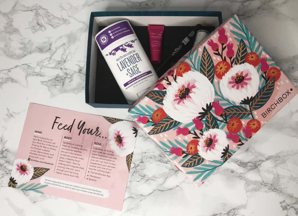 A floral Birchbox set on a marble surface, containing lavender sage deodorant, two small beauty products, and an informational card.