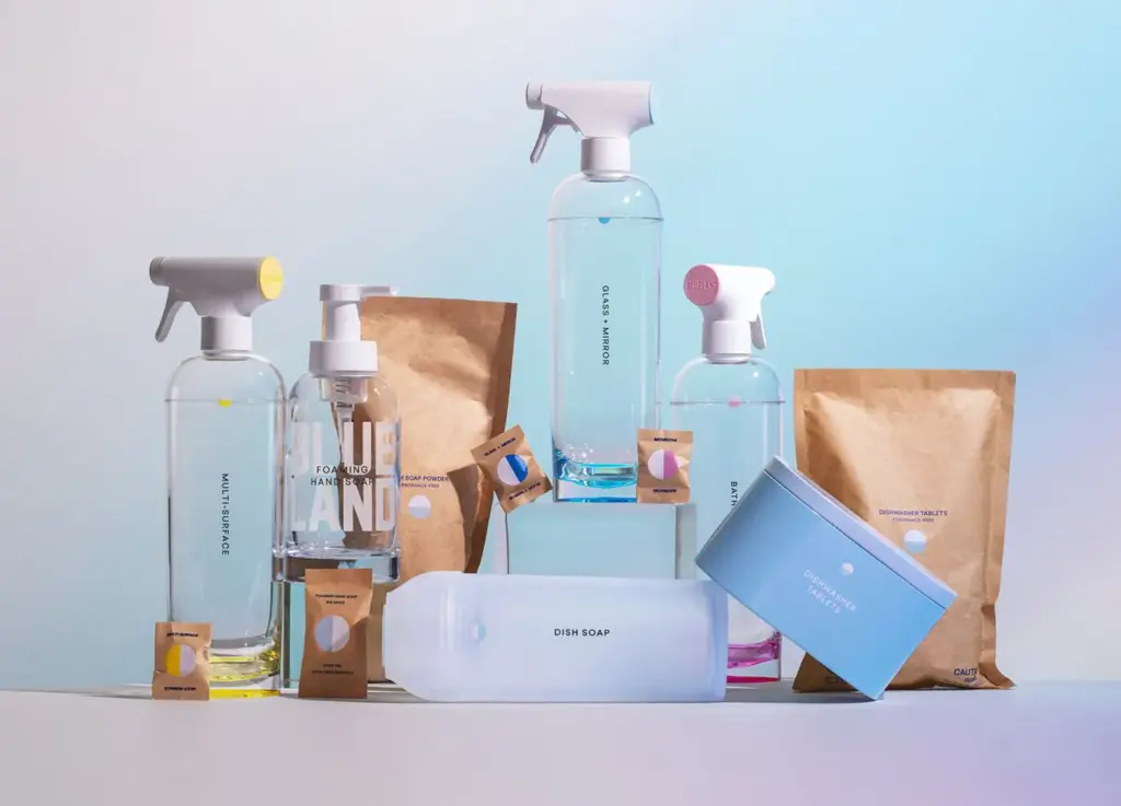 A collection of eco-friendly household products, including spray bottles, soap dispenser, and various packets, arranged on a surface with a gradient blue background.