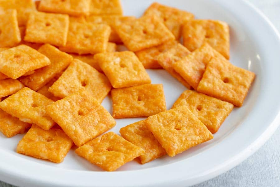 A white plate filled with square, orange cheese-flavored crackers.