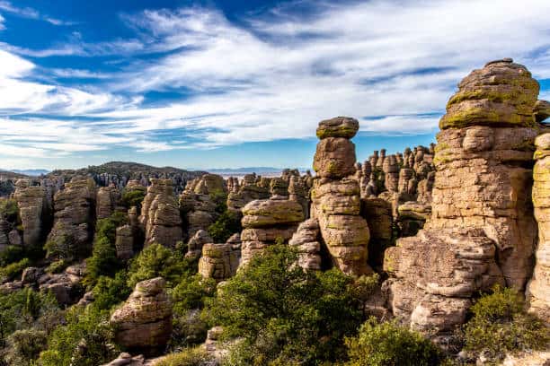 Rock formations and green vegetation under a blue sky with wispy clouds.