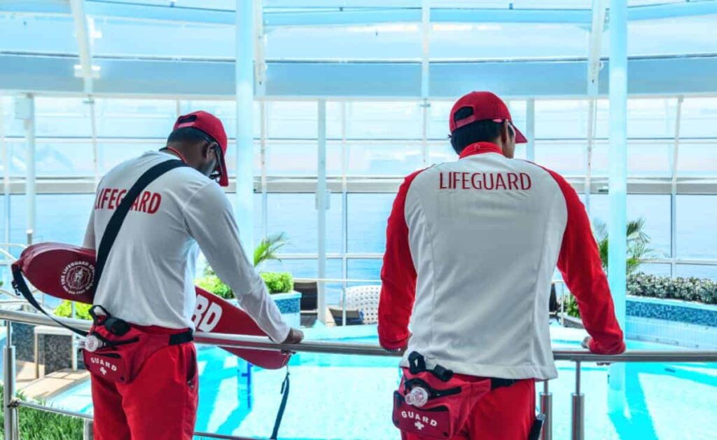 Two lifeguards in red and white uniforms stand by a pool, overlooking the water.