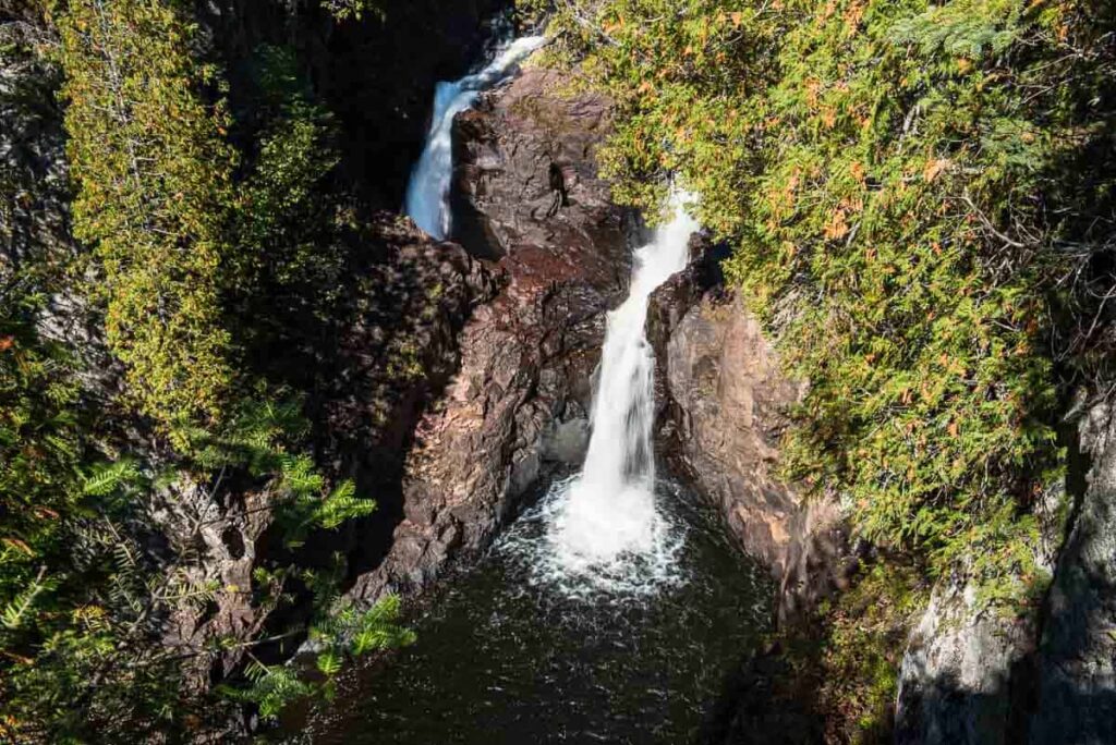 A narrow waterfall flows between rocky cliffs surrounded by dense green foliage.
