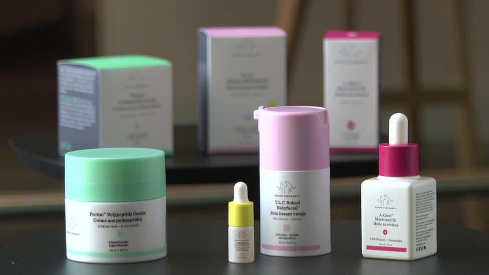 A variety of skincare products in colorful containers are displayed on a table, including jars, dropper bottles, and boxes.