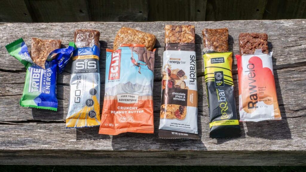 Seven assorted energy bars, reflecting the importance of nourishing foods in line with RFK Jr's health policies, are lined up on a wooden bench.