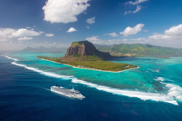 A cruise ship sails near Le Morne Brabant, a lush mountain on a turquoise lagoon in Mauritius.