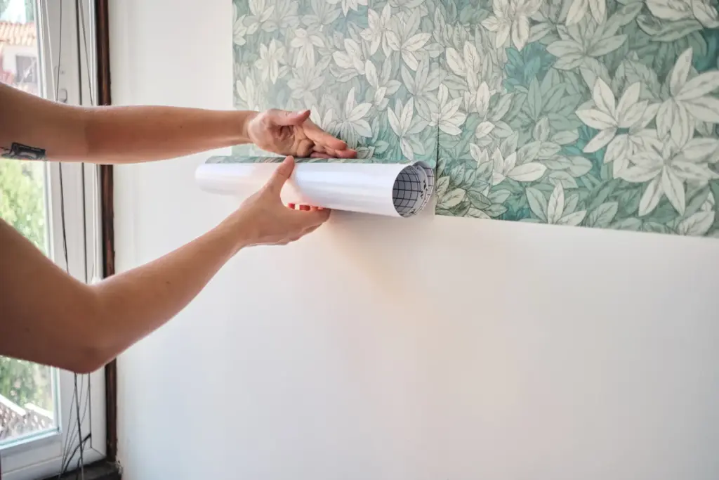 Person applying floral wallpaper to a white wall.